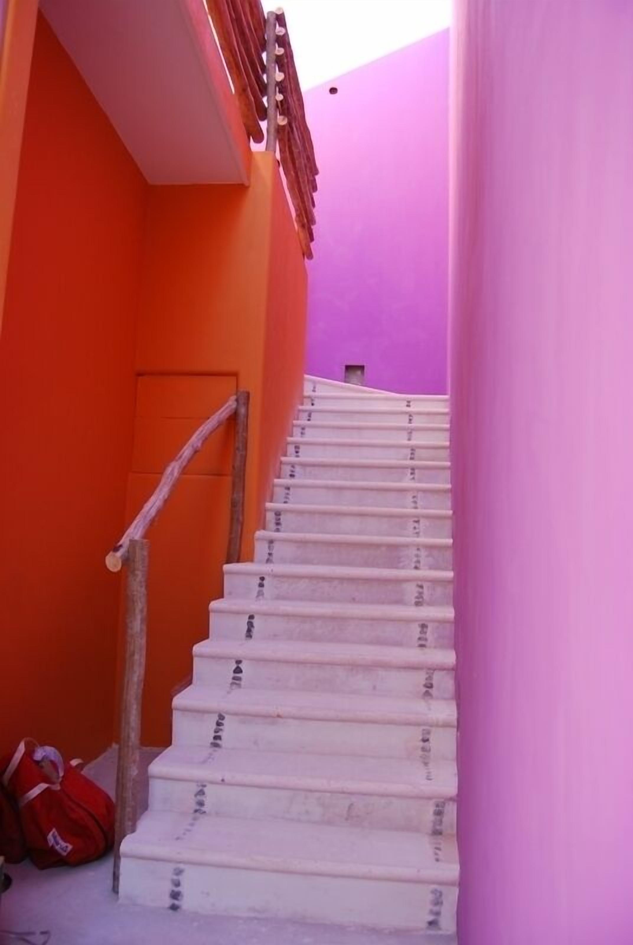 A staircase with white steps leading up to a door, surrounded by walls painted in bright orange and purple.