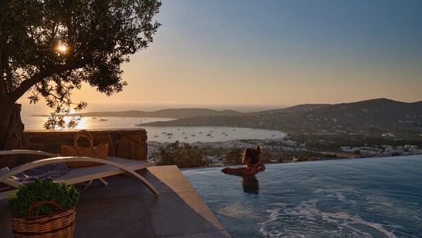 Ein Pool ohne Ende mit Blick auf das Meer und Boote, eine Lounge mit einem Baum und ein Korb mit Grünpflanzen.