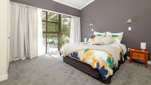 Ein Schlafzimmer mit einem großen Bett, einem Nachttisch, einer Lampe und Blick durch ein Fenster.