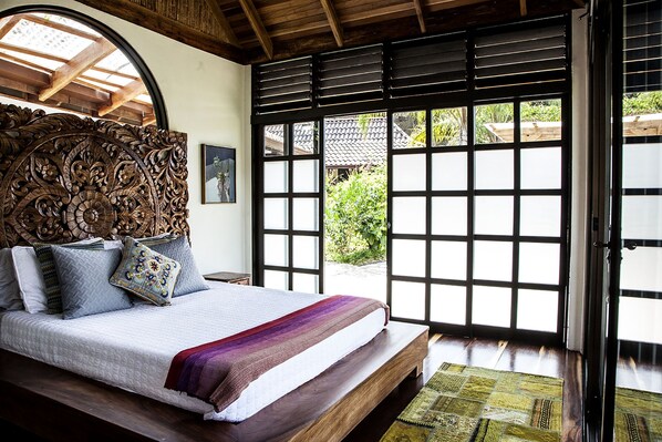 Ein Schlafzimmer mit einem großen Bett, einem Holz-Kopfende, Blick durch einen Shoji-Bildschirm und Holzboden.