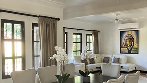 A spacious living room with a dark wooden dining table, white upholstered chairs, a white sofa, and a painting on the wall. - Experience the jungle of Costa Rica!! Direct oceanfront property for 8 guests. (Puntarenas)