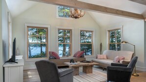 A spacious living room with a high ceiling, large windows, a fireplace, and a cozy seating area. - Lakeside life at its best! (Enfield)