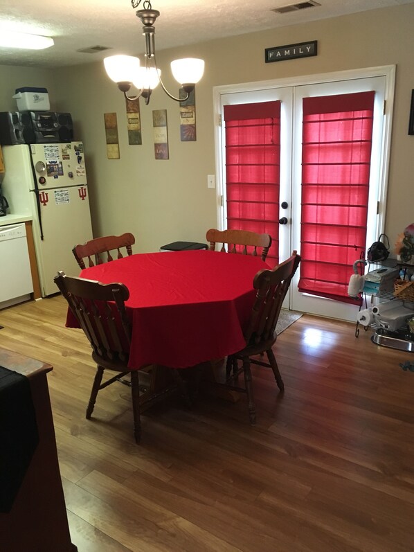 Un comedor con una mesa roja y sillas de madera, un refrigerador con imanes y una puerta con un cartel que dice 'FAMILIA'.