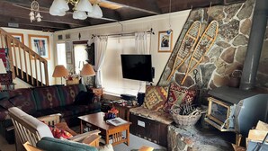 A cozy living room with a stone fireplace, a television, a sofa, and a wooden chair. - Year-Round Lake Tahoe Getaway -- Comfortable and Spacious! (South Lake Tahoe)