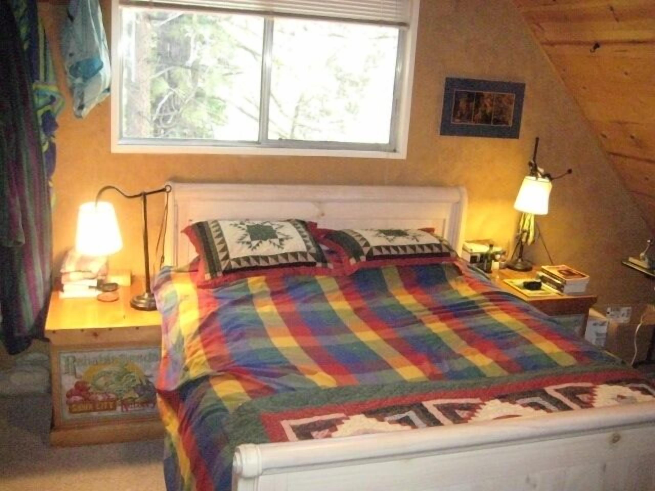Une chambre à coucher avec un lit, deux lampes de chevet, une fenêtre et un tableau accroché au mur.