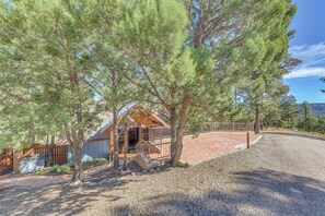 A cabin with a wooden deck, surrounded by trees and a gravel driveway.