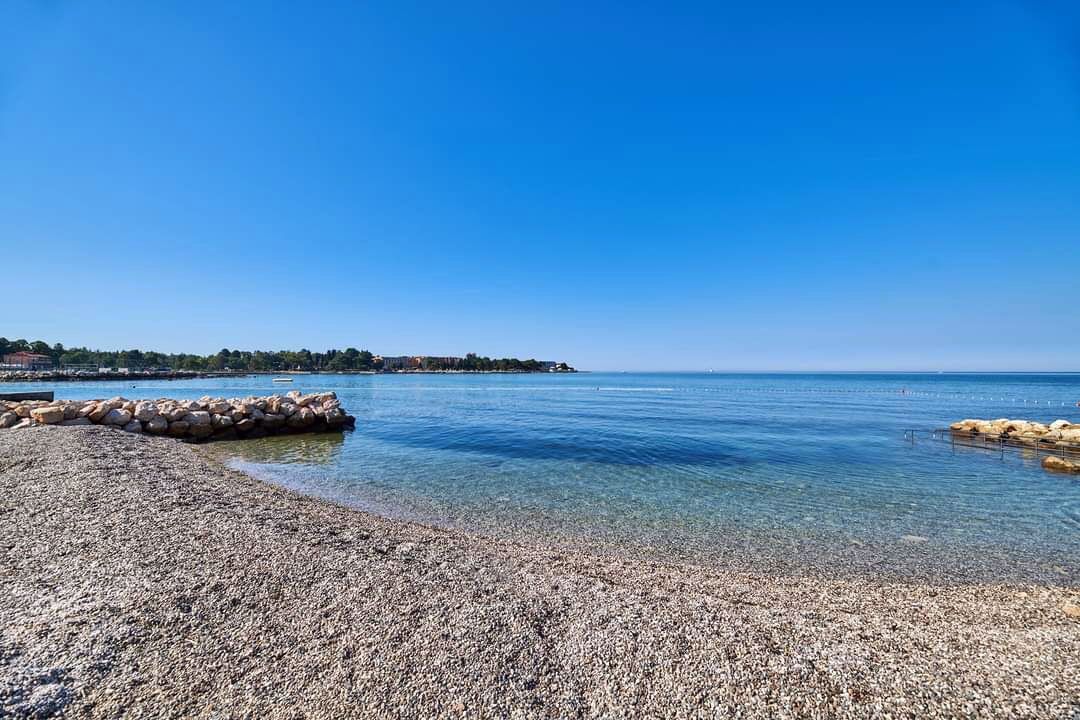 Een kiezelstrand met helder water en een rotsachtige kustlijn.