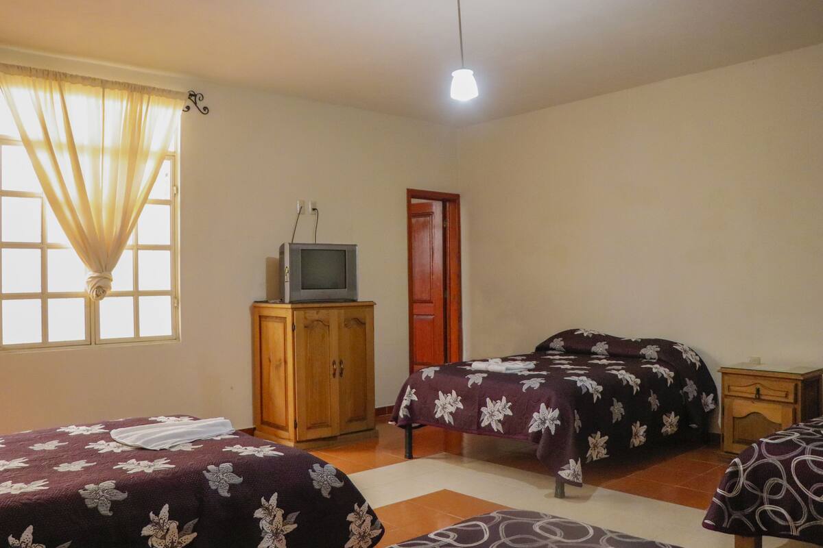 A bedroom with two beds, a wooden cabinet, a television, and a window with curtains.