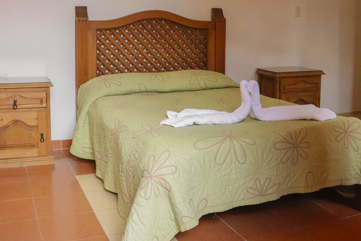 A bedroom with a wooden bed frame, green floral bedding, and a nightstand with a lamp.