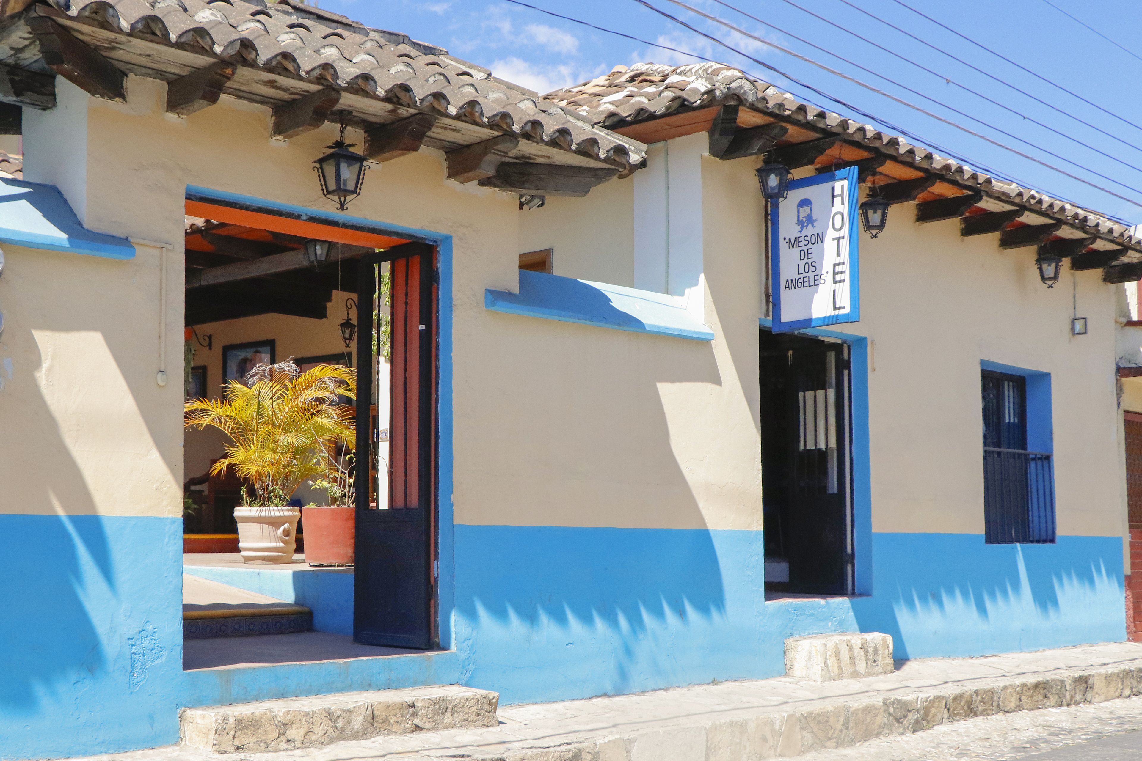A hotel with a blue and beige facade, a tiled roof, and a sign indicating it is the "Meson de los Angeles."