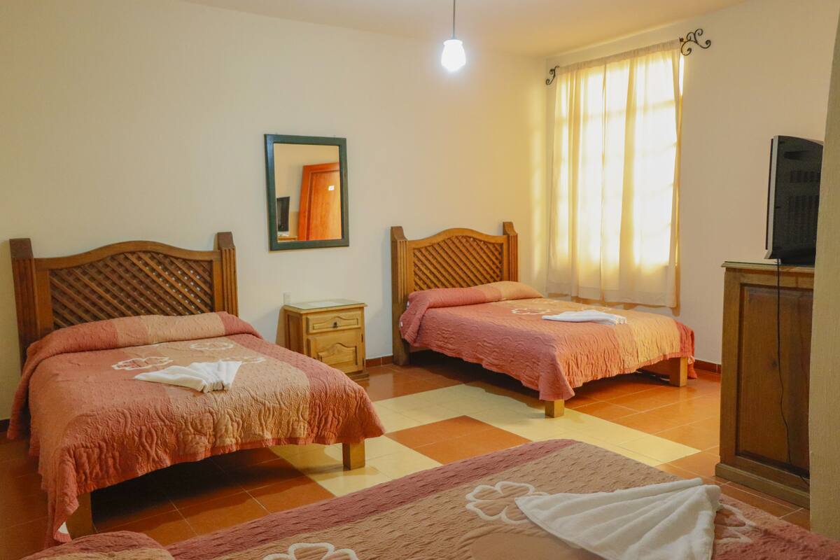 A hotel room with two beds, a small bedside table, a television, and a window with curtains.