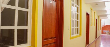 Un pasillo con puertas y ventanas, piso de baldosas y techo con una lámpara.