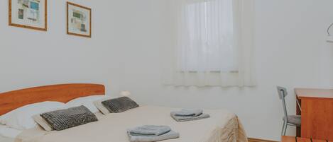 A neatly made bed with pillows and folded towels, a wooden desk, and two framed pictures on the wall.
