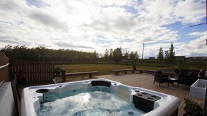 A hot tub on a wooden deck with a picnic table and chairs nearby. - Hestaland Riverside Cottage (Borgarbyggd)