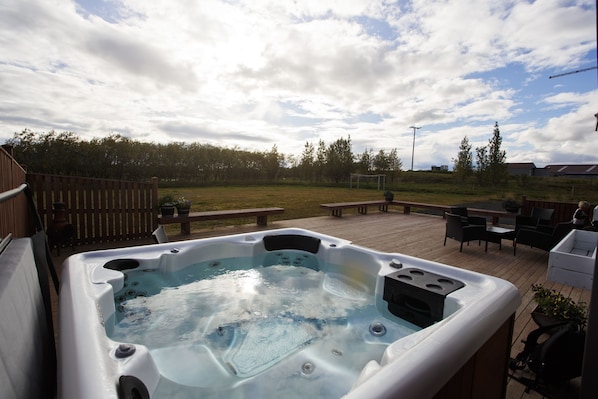 A hot tub on a wooden deck with a picnic table and chairs, surrounded by a fence and trees. - Hestaland Riverside Cottage (Borgarbyggd)