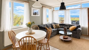 A modern living room with a dining area, large windows, and a view of the outdoors. - Hestaland Riverside Cottage (Borgarbyggd)