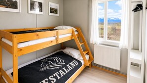 A bunk bed with a black mattress cover featuring a horse logo and the word 'HESTALAND'. There are three framed pictures on the wall, a window with curtains, and a white wardrobe. - Hestaland Riverside Cottage (Borgarbyggd)