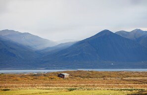 A rural landscape with mountains, a small house, and a body of water. - Hestaland Riverside Cottage (Borgarbyggd)