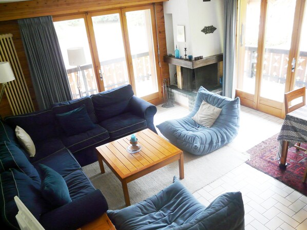 A living room with a dark blue sofa, a blue bean bag chair, and a wooden coffee table. There is a fireplace with a mantel and a rug on the floor.
