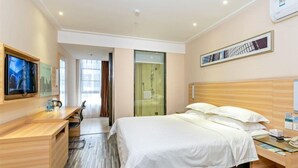 Ein modernes Hotelzimmer mit einem großen Bett, einem Schreibtisch, einem Fernseher und einer Duschkabine aus Glas.