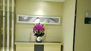 Ein Empfangsschalter mit einer Vase voller violetter Blumen, einem Bilderrahmen darüber und einem Schild mit der Zimmernummer.