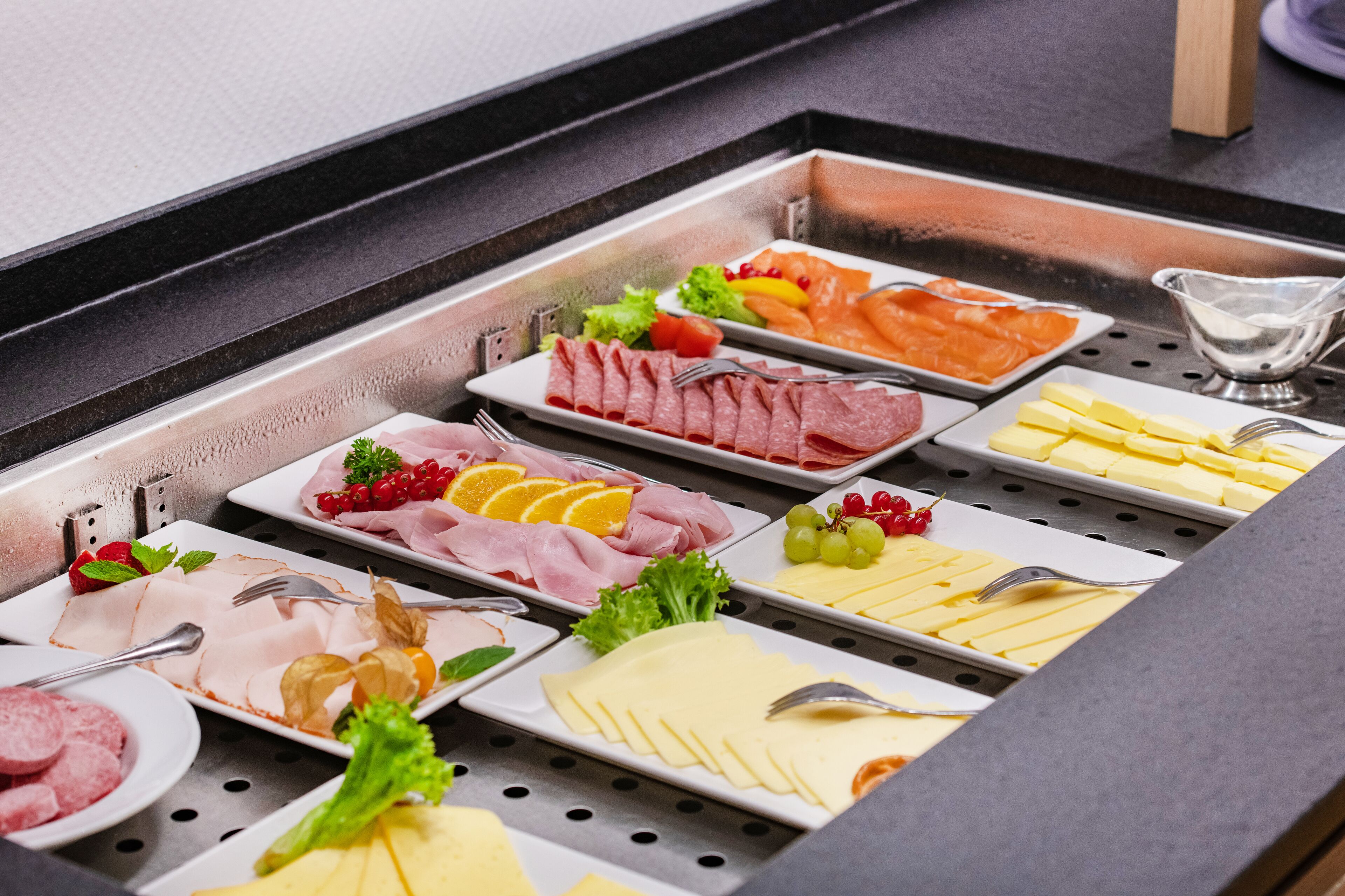 A buffet with various food items including meats, cheeses, and fruits.