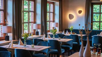 Un restaurant avec de nombreuses tables, des chaises bleues et de grandes fenêtres ornées de rideaux.