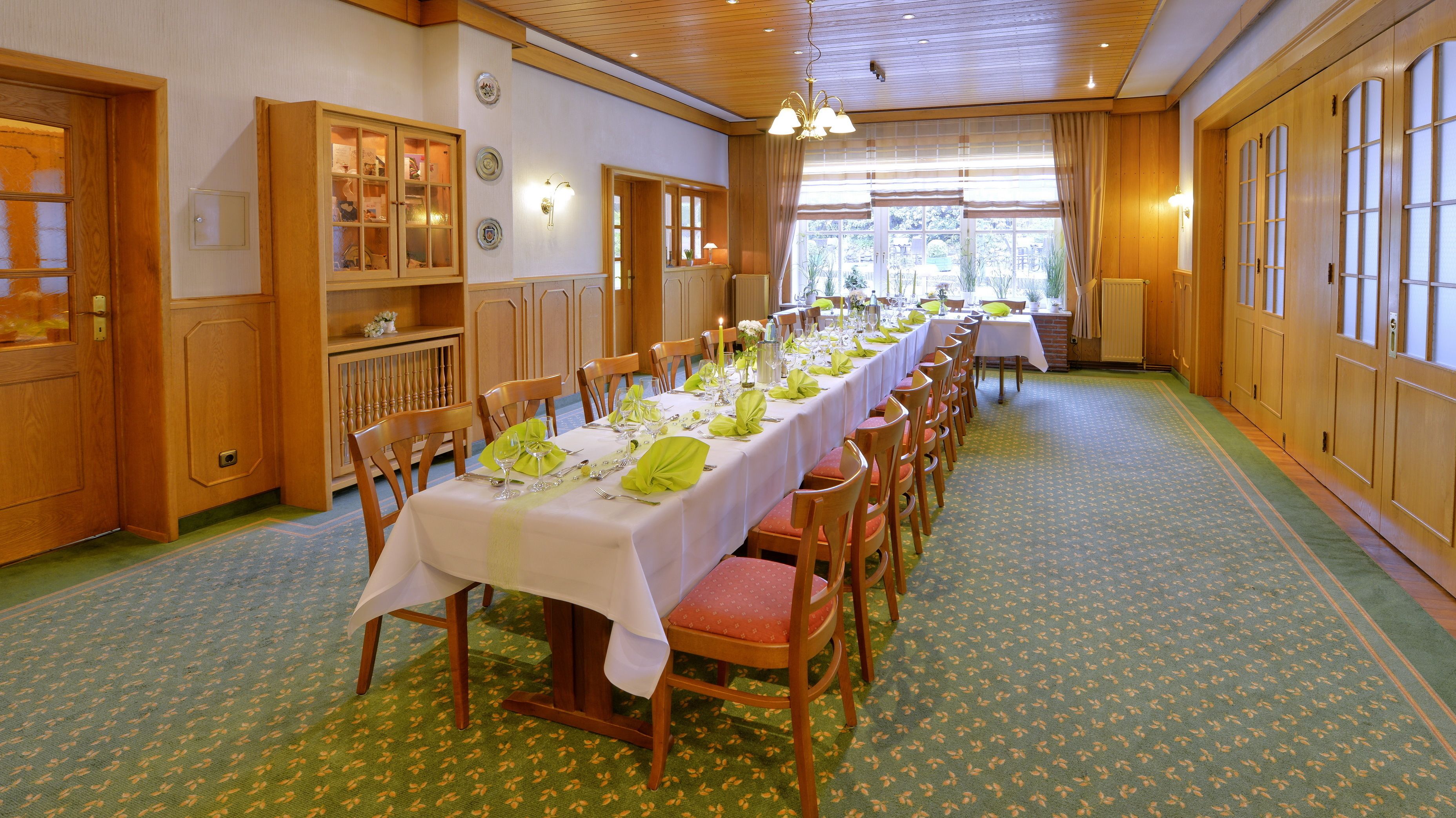 A long dining table set for a meal with chairs, wooden cabinets, and a patterned carpet.