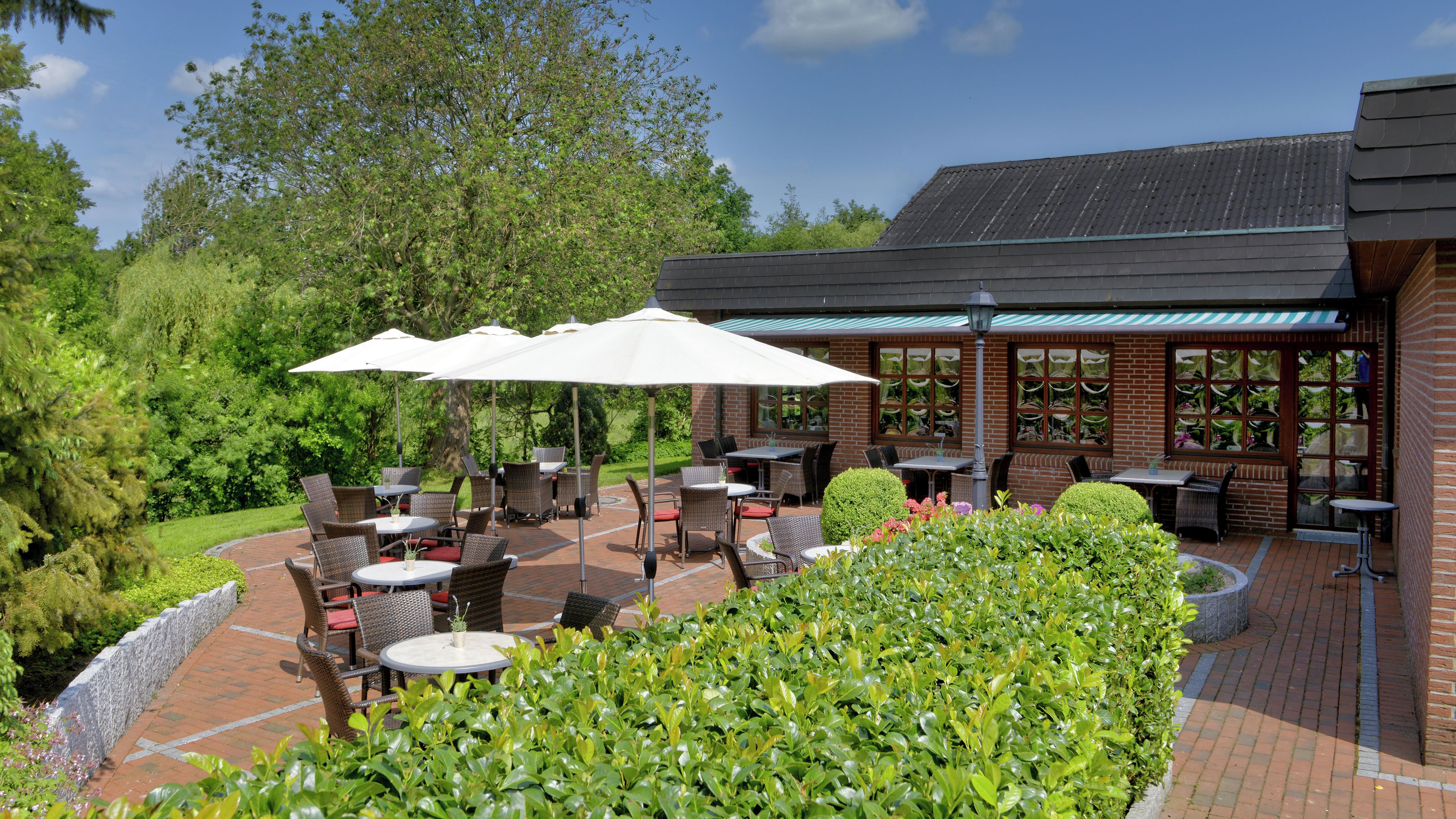 An outdoor patio with tables and chairs, surrounded by greenery and a brick wall.
