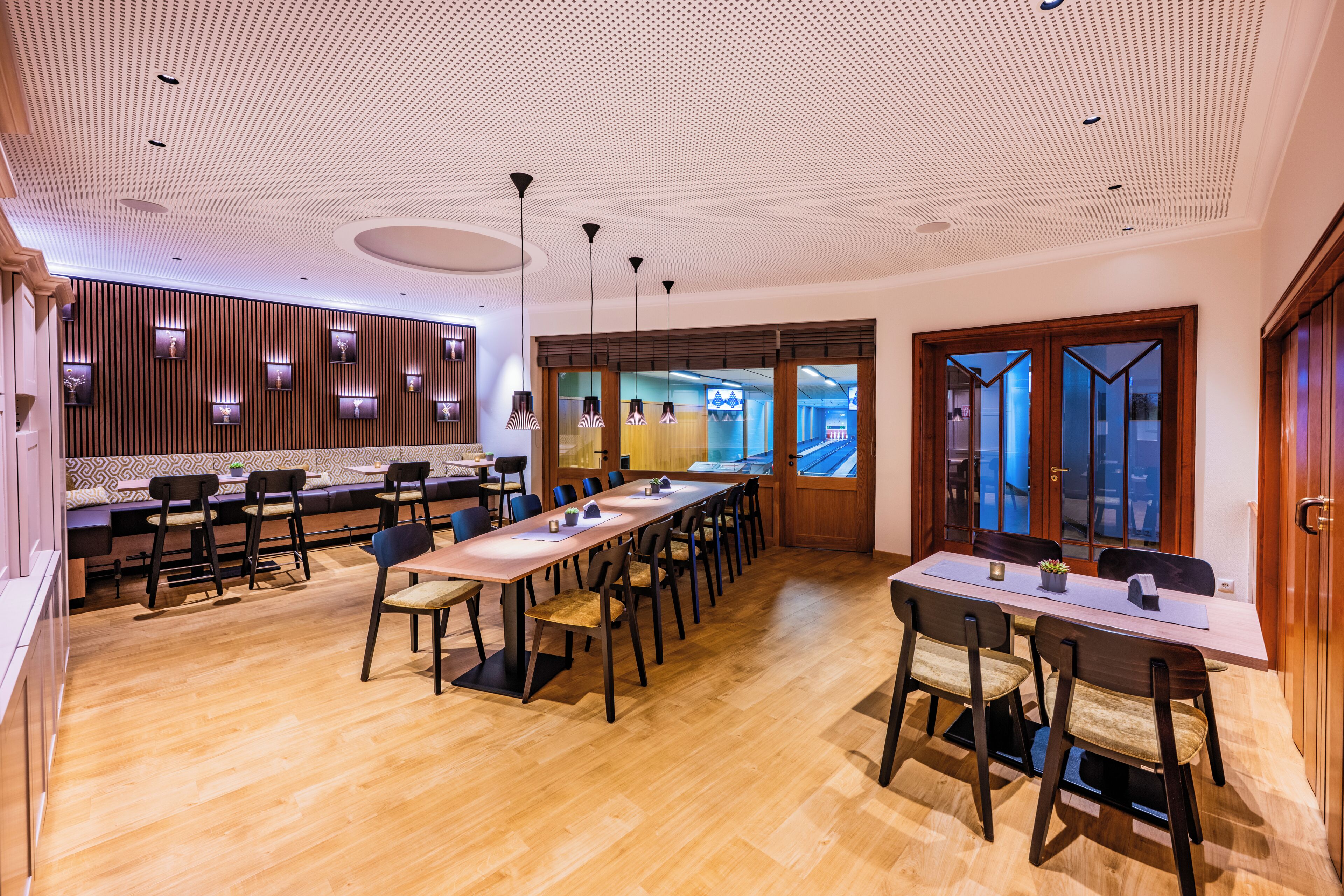 Un moderno vestíbulo de hotel con una larga mesa de comedor, múltiples sillas, una zona de recepción con mostrador y un muro con diseño.