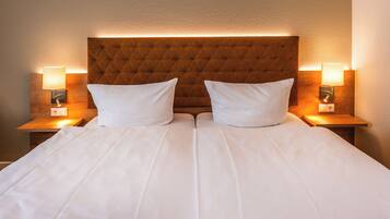 Een tweepersoonsbed met een gestoffeerd hoofdeinde, twee bedlampjes en een neutrale wand.