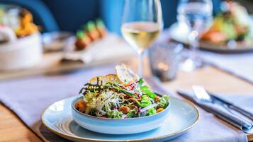 A dining table with a plate of salad, a glass of white wine, and a fork and knife on a napkin.
