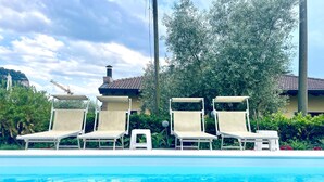 Un espace piscine avec des chaises longues, une piscine à l’eau d’un bleu limpide et, au fond, un bâtiment doté d’un toit recouvert de tuiles.