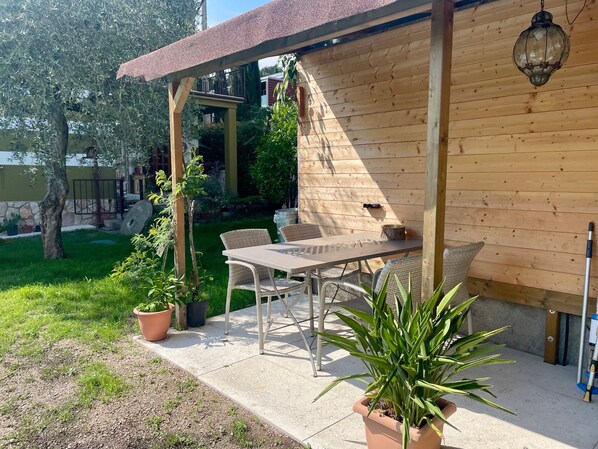 Une terrasse couverte avec une table et des chaises, entourée de plantes en pot et d’un mur en bois.