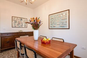 A dining room with a wooden table, chairs, a vase with flowers, and framed pictures on the wall.
