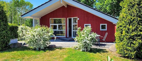 Ein rotes Holzhaus mit geneigtem Dach, großen Fenstern und einer kleinen Veranda mit Stühlen.