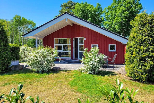 Een rood houten huis met schuine dak, grote ramen en een klein terras met stoelen.