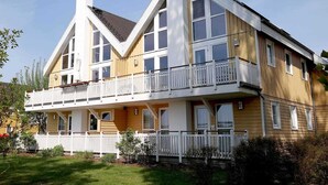 A two-story house with a balcony, a chimney, and a white fence.