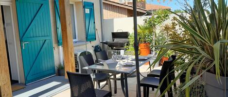 An outdoor patio with a table set for dining, surrounded by chairs, and a grill.