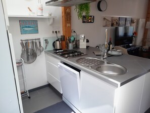 Eine moderne Küche mit Edelstahlgeräten, einem Geschirrspüler und einer Spüle. An den Wänden befinden sich Küchenutensilien, eine Pflanze und Kunstwerke.