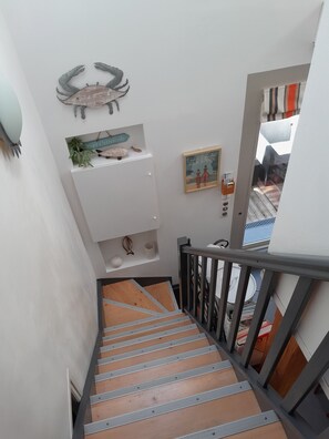 Eine Treppe mit Holzvertäfelung und Metallgeländern, die zu einer Zwischenebene mit einer dekorativen Wandverkleidung und einem gerahmten Bild führt.
