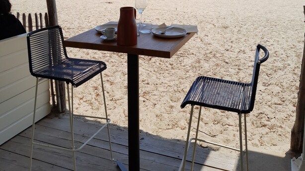 Una mesa con sillas frente a la playa, una terraza de madera y vista al mar.