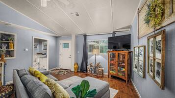 Un salon avec un canapé gris, un meuble en bois orné de cadres photos, une grande plante et un ventilateur de plafond.