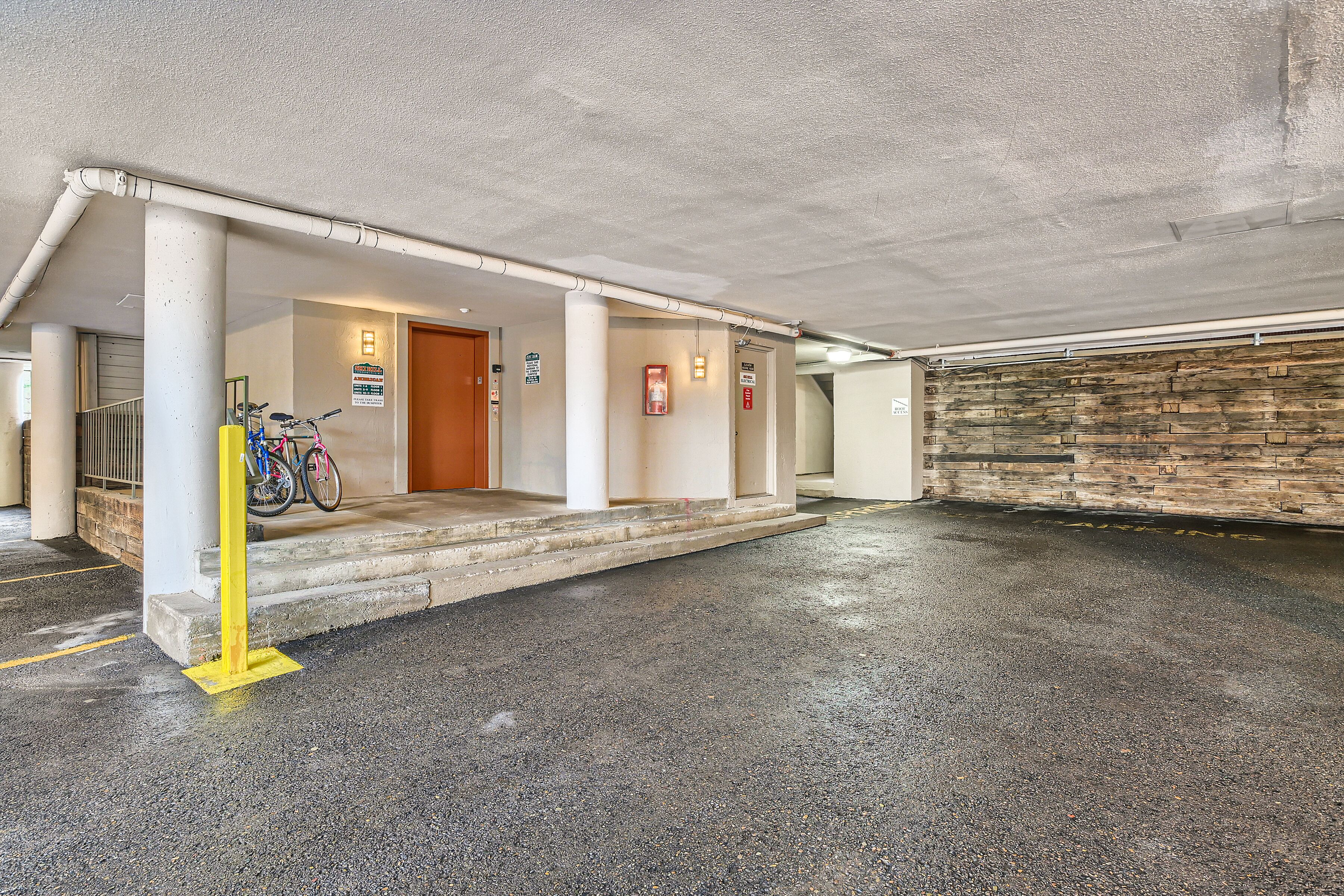 A covered parking area with a concrete floor, a yellow safety line, and a bicycle parked near the entrance.