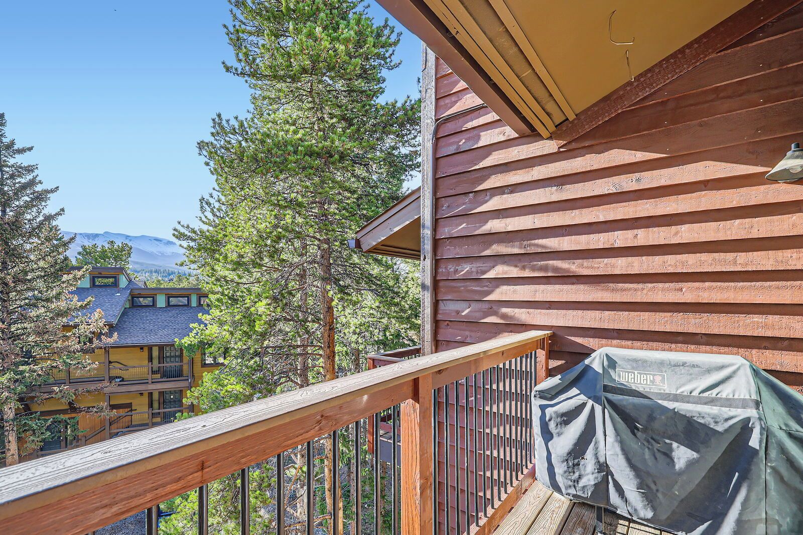 A wooden deck with a grill cover, a railing, and a view of a mountain and other buildings.
