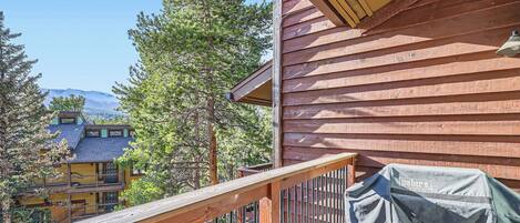 A wooden deck with a grill cover, a railing, and a view of a mountain and other buildings.