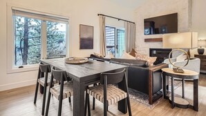 A modern living room with a dining area, large windows, a fireplace, and a stone accent wall. - Free SkyCard Act 2-Level Condo + Loft, Outdoor Pool/Hot Tubs-Lances West 7 (Breckenridge)