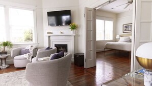Un salon spacieux doté d’une cheminée, d’un téléviseur à écran plat fixé au-dessus, et d’un coin salon confortable avec un canapé et des fauteuils.