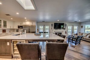 Una cocina amplia con una isla grande, un comedor con sillas, una sala de estar con un sofá y un televisor montado en la pared.