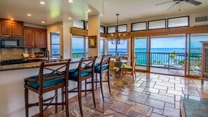 A spacious kitchen with a large island, wooden bar stools, and a view of the ocean through large sliding glass doors. - Dramatic Ocean Views - Fantastic Location - REDUCED RATES! (Kapalua)